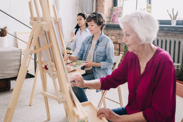Portrait of art students sitting in row and painting at easels in art studio, focus on smiling ...
