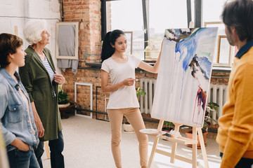 Portrait of pretty young woman presenting modern watercolor painting to audience standing in...