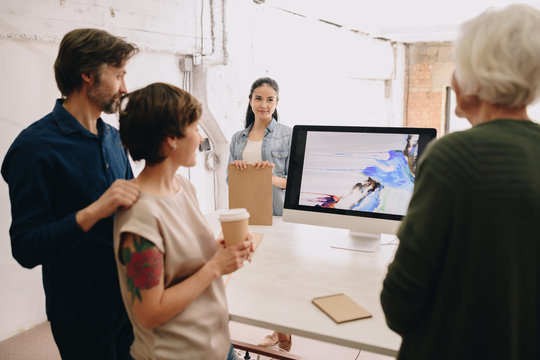 Group of modern creative people looking at computer screen with abstract painting in design studio, copy space