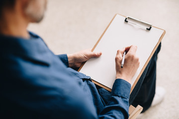 Obraz premium Warm toned closeup of unrecognizable mature man holding blank sheet of paper ready to write or sketch pictures, copy space