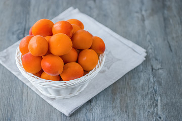 Ripe bright apricots in white basket on gray wooden background.