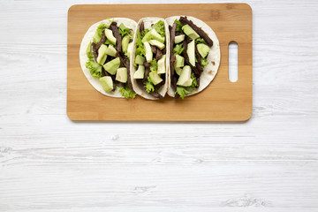 From above, tortillas with grilled beef and avocado on the bamboo board over white wooden surface. From above, overhead. Copy space.
