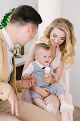 Beautiful young parents smile with their one-year-old child at home in a beautiful interior in pastel colors. Family look. Happy birthday party