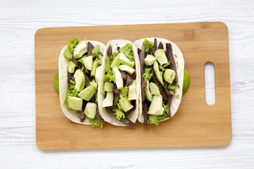 Tortillas with grilled beef, avocado and lime on the bamboo board over white wooden surface. View from above, overhead, flat-lay.