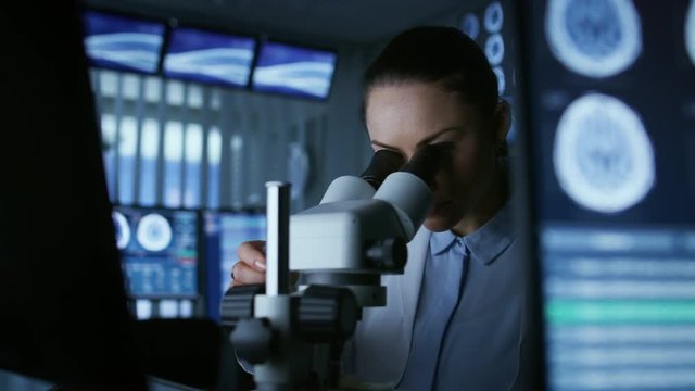 Female Medical Research Scientist Looking Through the Microscope Types Acquired Data in the Computer. Shot on RED EPIC-W 8K Helium Cinema Camera.