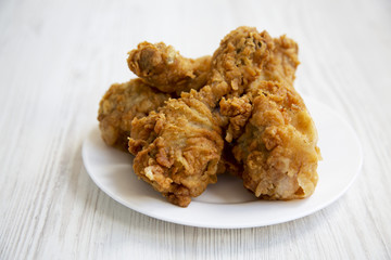 Fried chicken legs on a white round plate over white wooden surface, closeup. Side view.