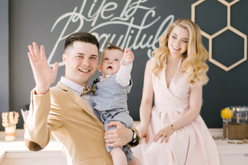 Beautiful young parents smile together with their one-year-old child at home in a beautiful interior in pastel colors with a festive blue cake. Family look. Happy birthday party. Selection focus