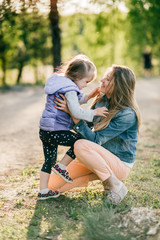 Fototapeta premium Happy smiling mother hugging her lovely little daughter outdoor. Lifestyle family. Adult cheerful female parent playing with her beautiful emotional child at nature in summer. Positive people faces.