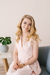 Portrait of a beautiful young girl with curly blonde hair. Sits at home in a beautiful interior and smiles