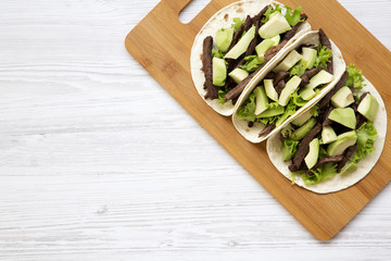 Tortillas with grilled beef and avocado on the bamboo board on a white wooden table. Top view, from above, overhead. Copy space.