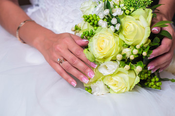 Wedding ring on finger of bride, keeping wedding bouquet of white roses