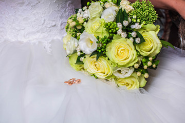 Wedding gold rings near bouquet of roses on wedding dress, closeup