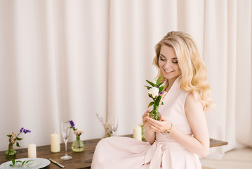 Portrait of a beautiful young girl with curly blonde hair in a delicate dress on a light background. Eyes look down with beautiful makeup closeup