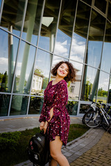 Fototapeta na wymiar Happy girl with curly hair standing near a glass building