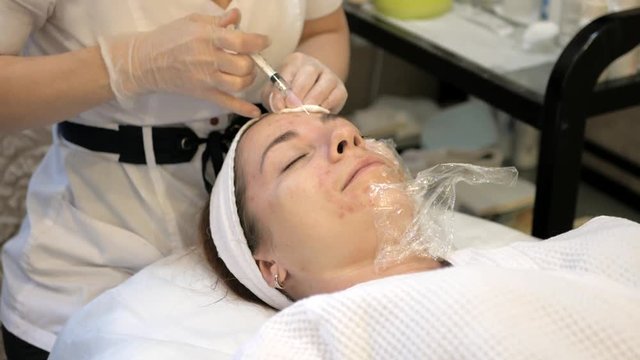 Rejuvenating facial injections, young girl at cosmetologist procedure, doctor hands in gloves make face aging injections in female facial skin, close up. Cosmetology, Spa or beauty salon, 4K