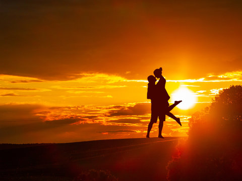 Romantic couple on countryside at the sunset with the sun and one tree