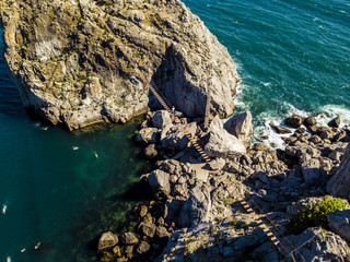 unrecognizable man walking on the rope bridge over the sea water aerial view
