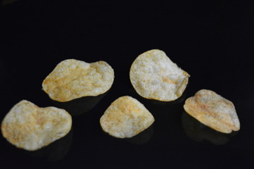 On a black glossy background are located fragrant salty fresh potato pips with cheese taste with reflection