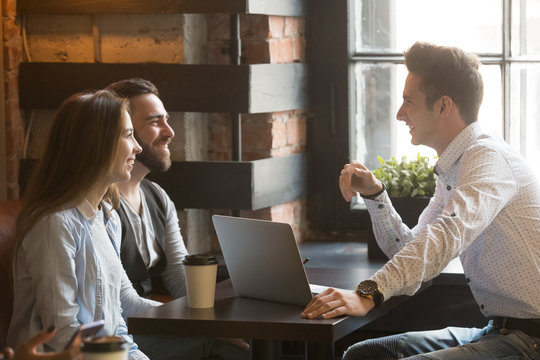 Male architect talking to smiling millennial couple, consulting on housing project, realtor explaining mortgage and contract condition to excited young couple during friendly meeting in coffee shop