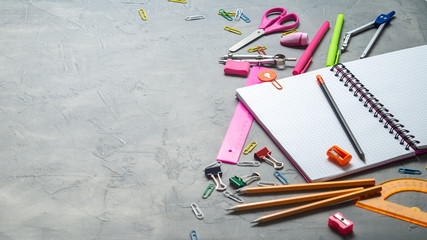 Preparations for school: A large white notepad, pencils, a pink ruler, scissors and other consular accessories on a gray background.