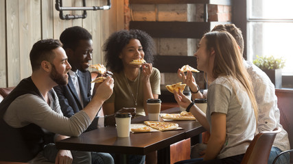 Smiling multiracial friends eating pizza and drinking coffee, laughing and having fun in...