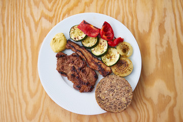 Fototapeta na wymiar Barbecue or grilled pork meat consist from pork collar and streaky bacon served with grilled vegetables, zucchini, onion, red pepper and whole grain bread and mustard. 