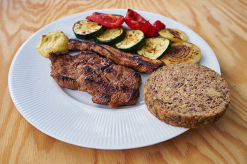 Detail of grilled pork meat consist from pork collar and streaky bacon served with grilled vegetables, zucchini, onion, red pepper and whole grain bread and  mustard.