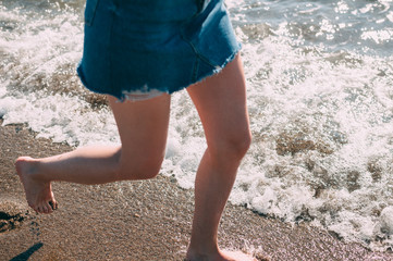 Young girl runs along the sea sandy beach barefoot, concept, legs.