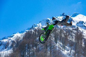 racer on a motorcycle in flight, jumps and takes off on a springboard against the snowy mountains