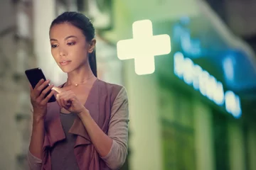 Photo sur Aluminium Pharmacie une jeune femme asiatique localise une pharmacie la nuit avec son téléphone intelligent. Communiquer sur les pharmacies ouvertes pendant la nuit, en utilisant la navigation pour les localiser, la santé, l& 39 astreinte