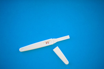 Pregnancy test with a positive result lying on a blue background.