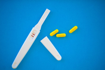 The result is positive. Close up of pregnancy test and contraceptive pills birth control concept on blue background