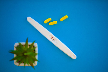The result is positive. Close up of pregnancy test and contraceptive pills birth control concept on blue background