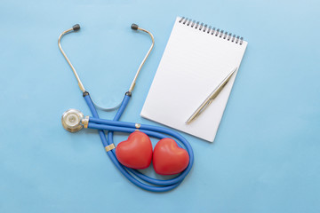 Cardiologist's day; doctor's day; heart disease; Cardiology, blue stethoscope with two red hearts, a notebook and a pen on a blue background; diagnosis of heart disease
