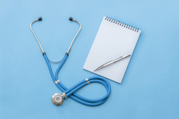 Cardiologist's day; doctor's day; heart disease; Cardiology, blue stethoscope with notebook and pen on a blue background; diagnosis of heart disease; happy cardiologist's day