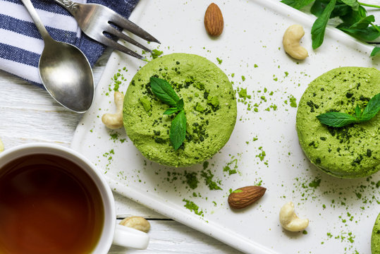 green matcha and banana vegan raw cheesecakes with mint and nuts over white wooden table with cup of tea and spoon