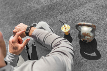 Gym fitness strength training fit man using sport watch smartwatch touchscreen at kettlebell weight lifting workout. green smoothie athlete healthy fitness lifestyle.