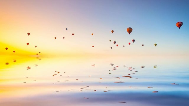 Hot air ballons reflected in ocean water fly in colorful sky at morning sunrise. Majestic summer landscape. Exploring beauty world, holidays and recreation. Travel background. Slow motion 4K footage