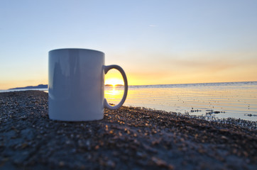 A blank white coffee mug on the shoreline of the great salt lake with a sunset through the handle. 
