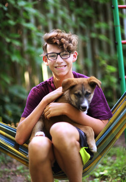 teenager boy hug puppy shepherd dog close up photo on green garden background