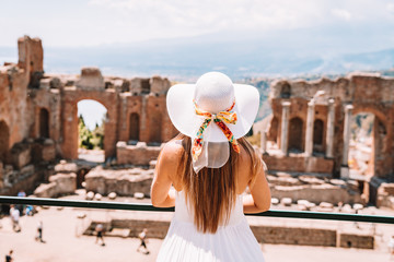Jule 04, 2018. Taormina, Italy. Beautiful girl in a long white dress and white summer hat sitting...