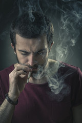 Young man inhaling a rich cloud of smoke, studio image, black background