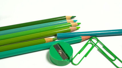 Green tones paper clips, colored pencils and pencil sharpener on white background