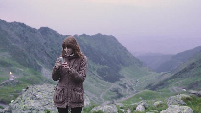 A young woman hiker climbs mountains and does selfie on smartphone camera. Transfagarasan, Carpathian mountains in Romania