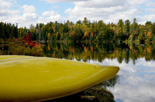 Autumn forest reflected in water beside yellow canoes. Colorful autumn morning in Ontario.