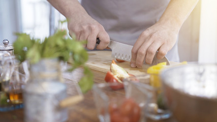 A close up of male chief cooker's hands cherry tomatoes on a wooden cutting board preparing salad