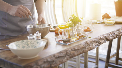Male chief cooker's hands mixing a salad with a spoon in a metal bowl on a kitchen table