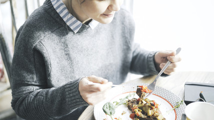A close up of female hands cutting a tartine of a stew salad on a bread lying on a plate in a cafe