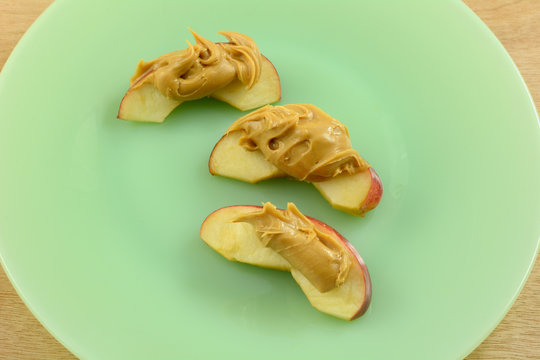 Close Up Of Apple Slices With Peanut Butter On Green Plate