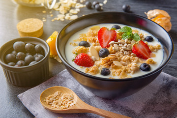 Warm light bowl of oat granola with yogurt, fresh strawberry, blueberries and nuts on black wooden table with copy space